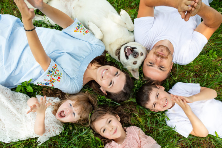 Happy beautiful big family together mother, father, children and dog lying on the grass top view